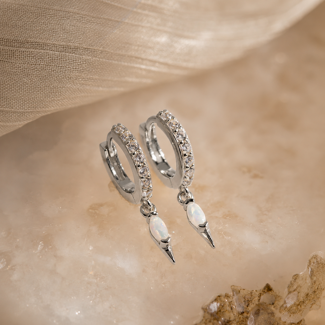 Silver hoop earrings with pearl-like drops on a beige fabric background